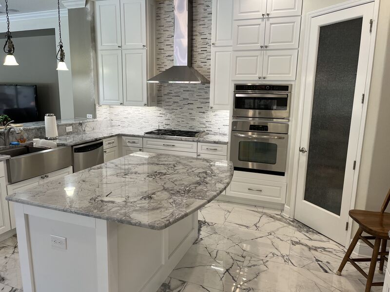 Remodeled kitchen with a quartzite island, white cabinetry and marble-look porcelain floor